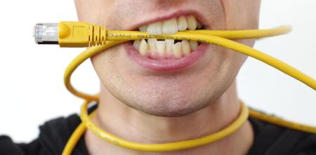 Detailaufnahme einer Person (Mundpartie), die ein gelbes Ethernet-Kabel um den Hals udn im Mund hat.