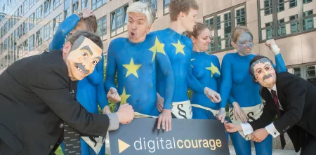 Mehrere nackt Menschen, die wie die Europa-Flagge angemalt sind (blau mit gelben Sternen). Daneben Menschen mit Masken. SIe halten ein Schild von Digitalcourage in den Händen.