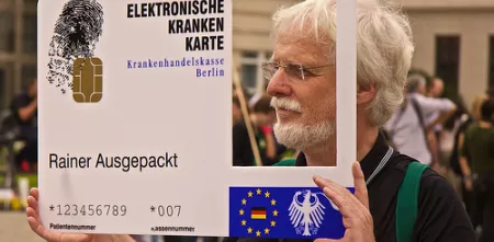 Ein Aktivist mit einer großen elektronischen Gesundheitskarte mit einem rechteckigen Loch auf der rechten Seite, wo ein Mensch durchschaut.