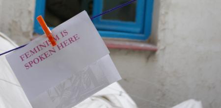 Ein Notizzettel an einer Wäschleine. Daruf steht: "Feminism is spoken here".