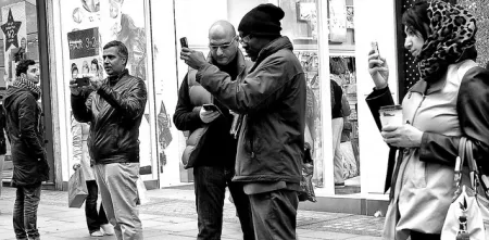 Menschen, die in einer Einkaufsstraße stehen und auf ihr Handy schauen (schwarz-weiß).