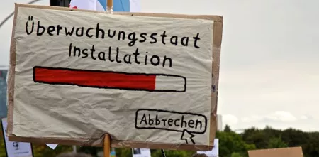 Demoschild mit einem Ladebalken und dem Text „Überwachungsstaat Installation“. Darunter ein Mauszeiger, der auf „Abbrechen“ klickt.