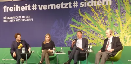 Mehrere Personen sitzen auf einem Podium. Im Hintergrund ein riesiger Banner: „freiheit #vernetzt# sichern“.