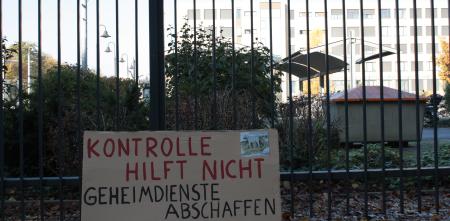 Ein Schild vor einem Zaun: „Kontrolle hilft nicht. Geheimdienst abschaffen.“