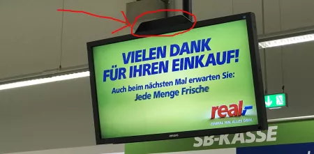Ein Bildschirm mit einem Werbetext von real,-. Eine kleine schwarze Box am oberen Bildschirmrand ist in rot eingekreist.