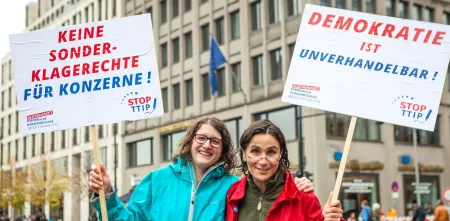 Zwei Demonstrant.innen mit Schildern, auf denen steht: „Keine Sonderklagerecht für Konzerne“ und „Demokratie ist unverhandelbar“.