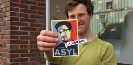 Eine Person hält einen Edward-Snowden-Asyl-Aufkleber Richtung Kamera.