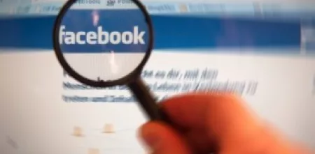 Eine Lupe lässt das Facebook-Logo auf einem Bildschirm größer erscheinen.