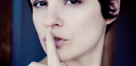 Eine Person, die ihren Zeigefinger vor den Mund hält.