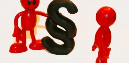 Zwei rote Plastikfigürchen. Eins hält das Paragraph-Symbol.