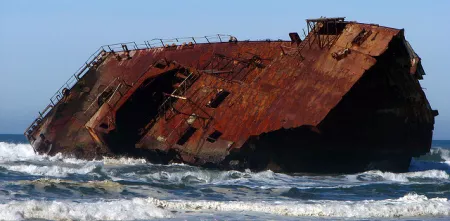Das Wrack eines Schiffes liegt auf der Seite in Ufernähe.