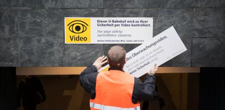 Eine Person von hinten, die ein Schild zur Videoüberwachung austauscht.