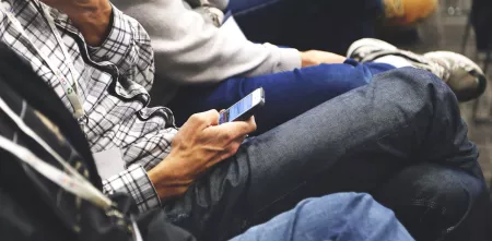 Mehrere Person sitzen in einer Reihe. Fokus auf ein Smartphone in der Hand.