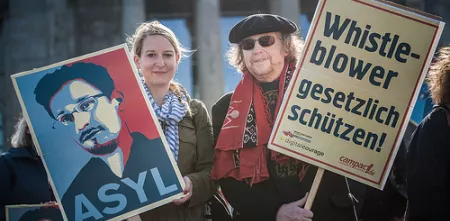 Zwei Personen mit Demo-Schildern: Edward Snwoden Asyl und Whistleblower gesetzlich schützen.