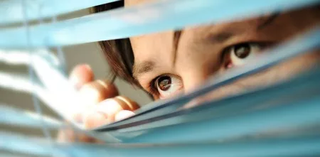 Eine Person, die durch ein Rollo schaut (Augen sind im Fokus).