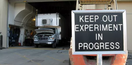 Eine Garage mit einem Truck. Davor ein Schild mit "Keep out. Experiment in progress."