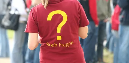 Eine Person von hinten. Auf dem roten T-Shirt ein gelbes Fragezeichen.