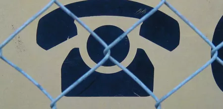 Symbol eines Telefons hinter Maschendrahtzaun.