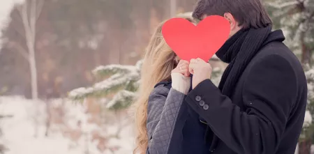 Zwei Personen die sich anscheinend küssen, verdeckt durch ein hochgehaltenes Herz.