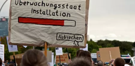 Demoschild mit einem Ladebalken und dem Text „Überwachungsstaat Installation“. Darunter ein Mauszeiger, der auf „Abbrechen“ klickt.