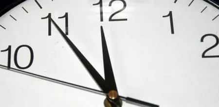 Eine Detailaufnahme einer Uhr mit dem großen Zeiger auf der elf und dem kleinen auf der zwölf.