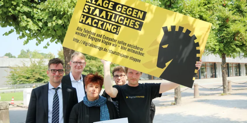 Rena Tangens und padeluun mit drei weiteren Personen, wovon eine ein Schild hochält: „Klage gegen staatliches Hacking“.