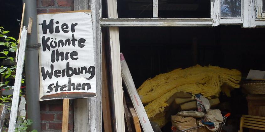 Eine vollgestellte Garage. Davor ein Schild mit dem Schriftzug: „Hier könnte ihre Werbung stehen“.