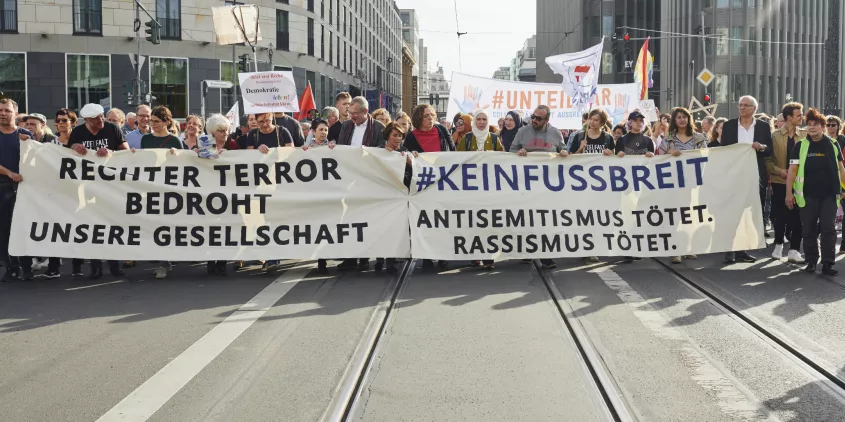 Viele Menschen auf einer Demo mit zwei Transparenten. Transparent 1: „Rechter Terror bedrohnt unsere Gesellschaft“; Transparent 2: „#KEINFUSSBREIT Antisemitismus tötet. Rassimus tötet.“