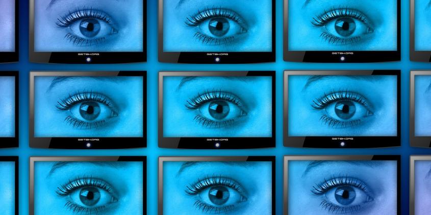Eine Wand voller Smart-TVs. Jeder Bildschirm zeigt ein großes, offenes Auge.