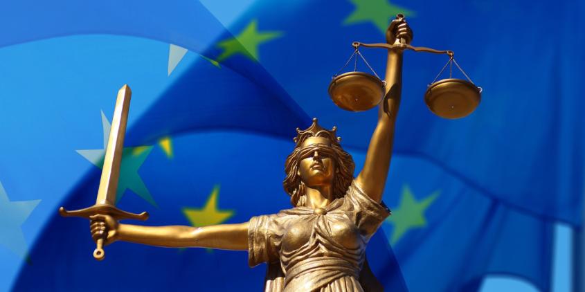 Justitia mit Schwert und Waage in Händen vor blauer EU-Flagge.