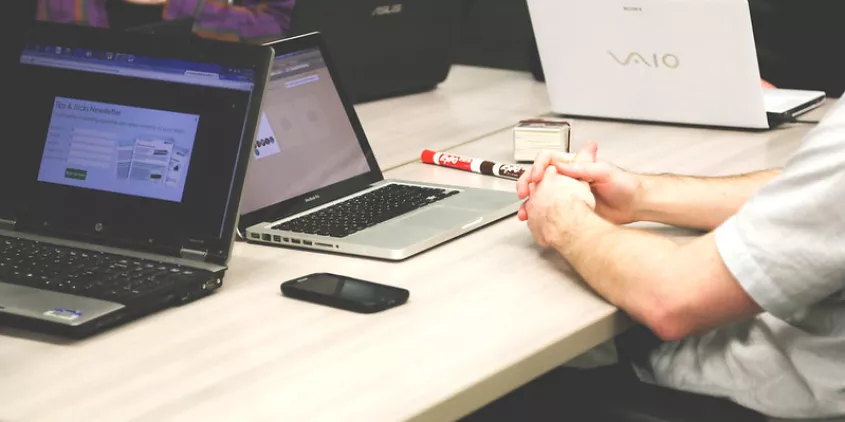 Foto von mehreren Personen, die mit ihren Laptops um einen hölzernen Tisch sitzen