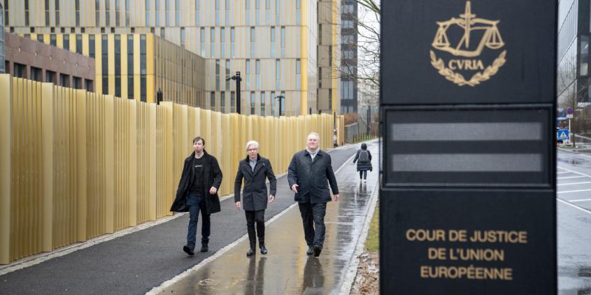Drei Personen laufen auf die Kamera zu. Rechts im bild ist ein Schild, welches den Europäischen Gerichtshof ausweist.