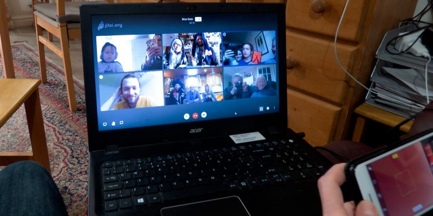 Laptop auf dem Schoß, darauf läuft eine Jitsi-Konferenz, eine Hand mit Smartphone ragt leicht ins Bild.
