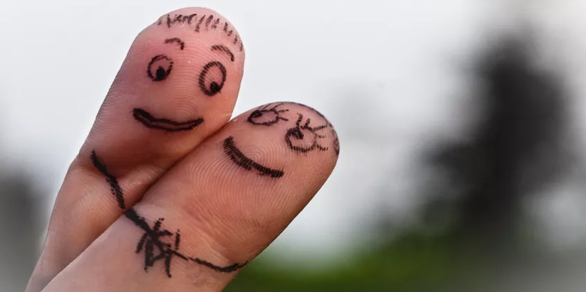 Zwei Finger haben verliebte Gesichter aufgemalt und flirten angeschmiegt miteinander.