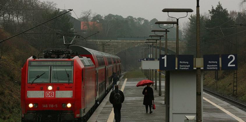 Ein roter Regionalzug an einem unüberdachten Haltepunkt an einem regnerischen Tag