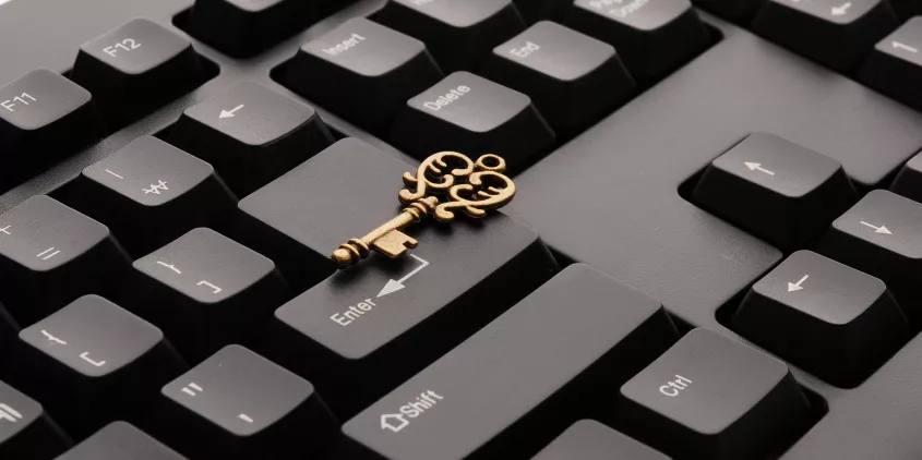 Ausschnitt einer schwarzen Tastatur. Darauf liegend ein goldener Schlüssel.