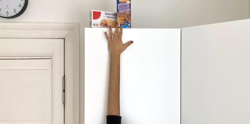 Foto eines Arms, der mit Hilfe eines Grafikprogramms künstlich verlängert wurde, um an Kekse zu kommen, die auf einem hohen Schrank stehen.