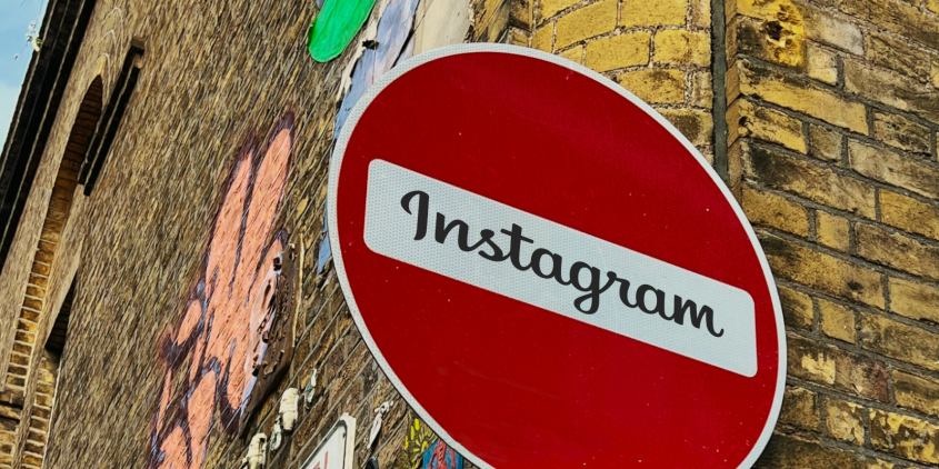 Detailaufnahme des Straßenschildes „Keine Durchfahrt“ (roter Kreis mit weißem Querbalken). Im weißen Bereich steht: „Instagram“. Im Hintergrund eine Klinkerwand mit Graffiti.