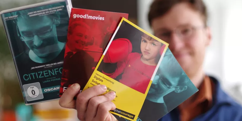 Eine Person, die Flyer und eine DVD (Citizenfour) Richtung Kamera hält:
