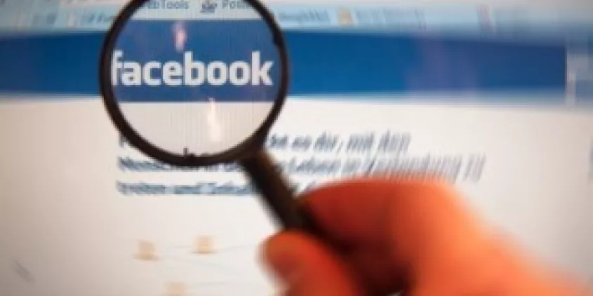 Eine Lupe lässt das Facebook-Logo auf einem Bildschirm größer erscheinen.