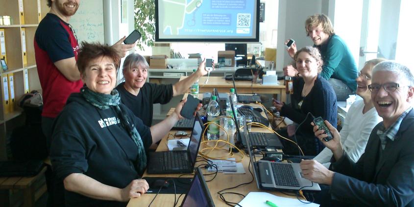 Teilnehmer.innen des Workshops "Free your Android" zusammen am Tisch mit Laptops und Smartphones.