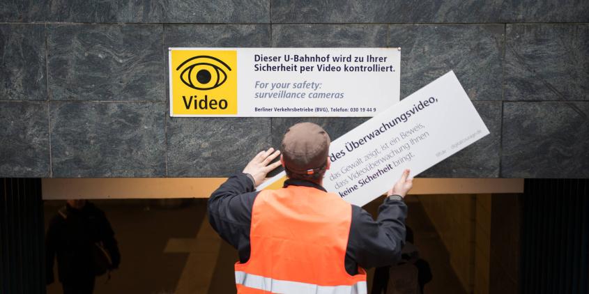 Eine Person von hinten, die ein Schild zur Videoüberwachung austauscht.