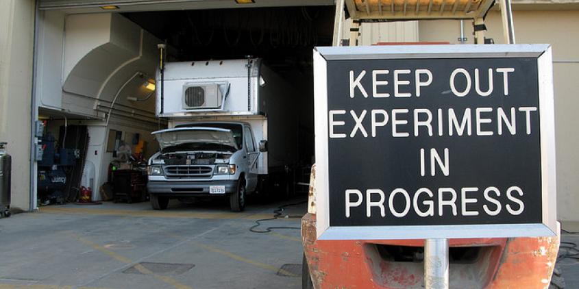 Eine Garage mit einem Truck. Davor ein Schild mit "Keep out. Experiment in progress."