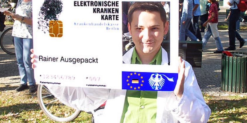 Ein Aktivist mit einer großen elektronischen Gesundheitskarte mit einem rechteckigen Loch auf der rechten Seite, wo ein Mensch durchschaut.