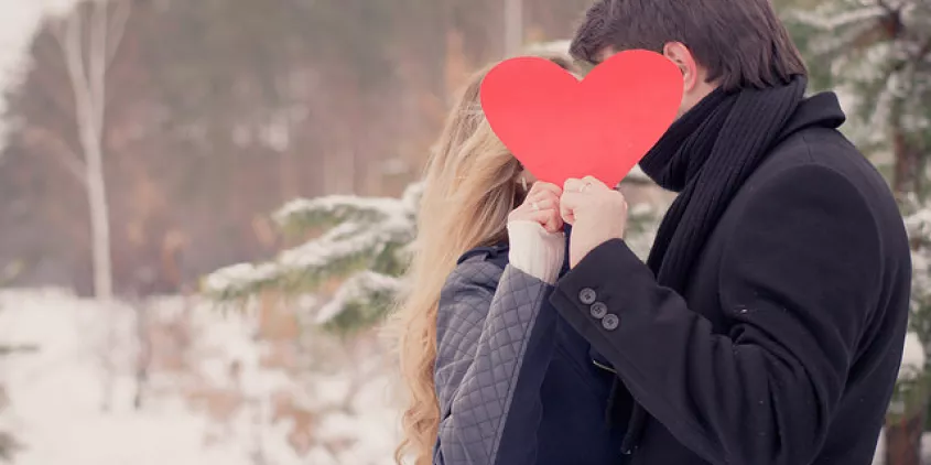 Zwei Personen die sich anscheinend küssen, verdeckt durch ein hochgehaltenes Herz.