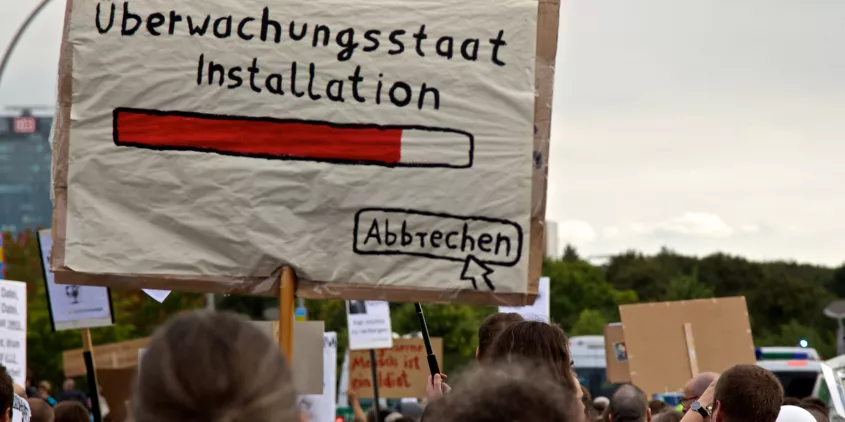 Demoschild mit einem Ladebalken und dem Text „Überwachungsstaat Installation“. Darunter ein Mauszeiger, der auf „Abbrechen“ klickt.