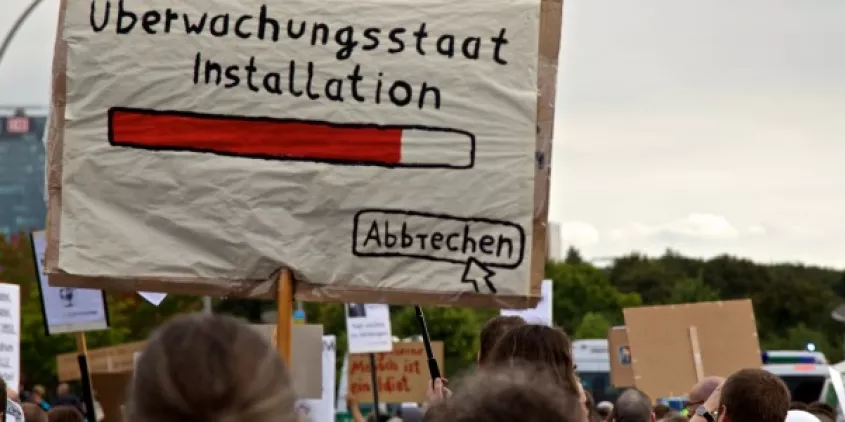Demoschild mit einem Ladebalken und dem Text „Überwachungsstaat Installation“. Darunter ein Mauszeiger, der auf „Abbrechen“ klickt.