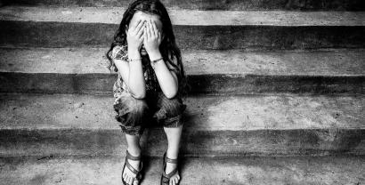 Ein Kind sitzt auf einer Treppe und hält sich die Hände vor das Gesicht (schwarz/weiß).