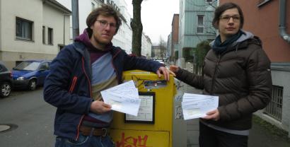 Offener Brief an VW, Uvex, AvD und Co: „VW muss Kinder-Tracking stoppen!“ Schutzranzen. Friedemann und Kerstin mit Briefen in der Hand vor einem Briefkasten.