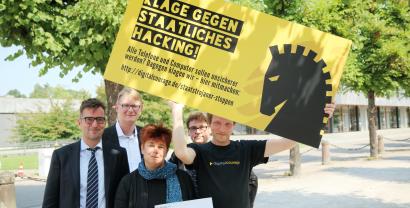 Rena Tangens und padeluun mit drei weiteren Personen, wovon eine ein Schild hochält: „Klage gegen staatliches Hacking“.